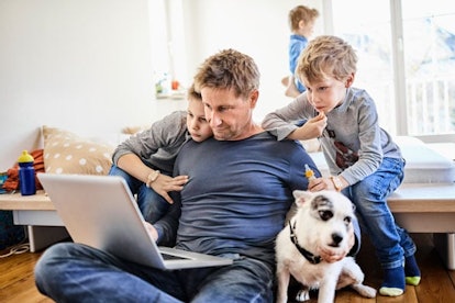 Father using laptop at home with children watching