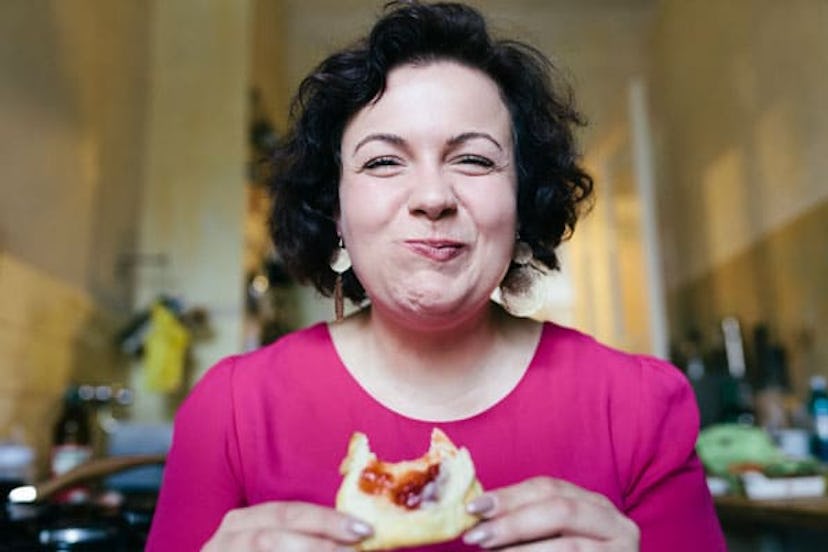 A woman smiling while enjoying her breakfast of jam on toast