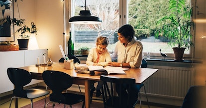 Mother assisting daughter in writing homework while sitting at home