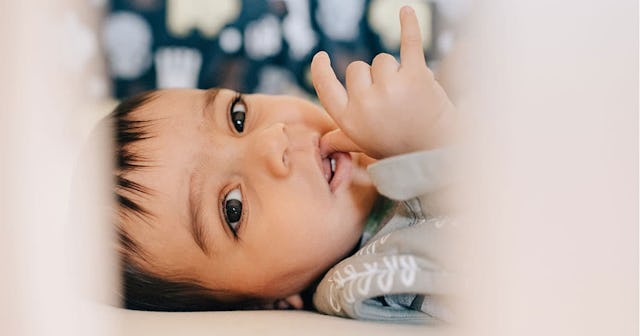 Baby boy lying awake and sucking thumb in crib