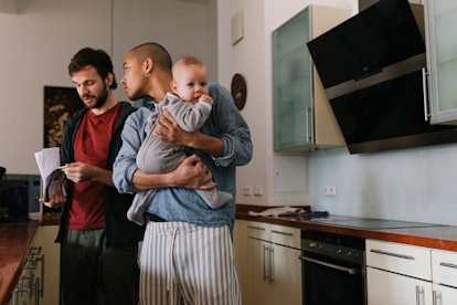 couple talking in kitchen, one of the Fathers is holding a baby in his arms.