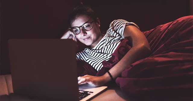 Woman lying in bed at home using laptop