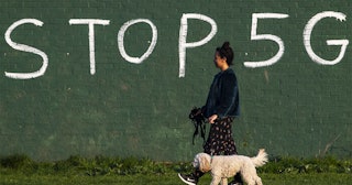 A woman walks her dog in-front of graffiti saying 'Stop 5G' on April 10, 2020 in London, England.