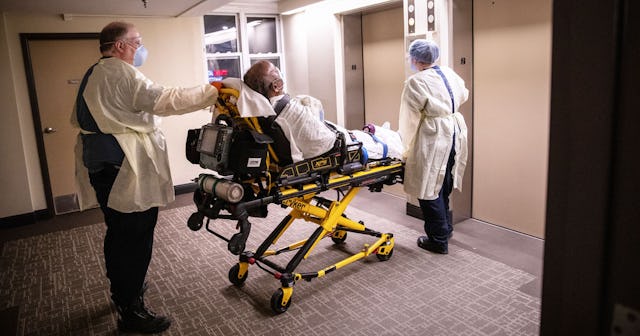 Medics wearing personal protection equipment (PPE), transport an African American patient showing CO...