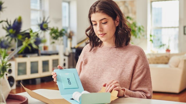 A woman opening a mint colored card box that has migraine medication in it