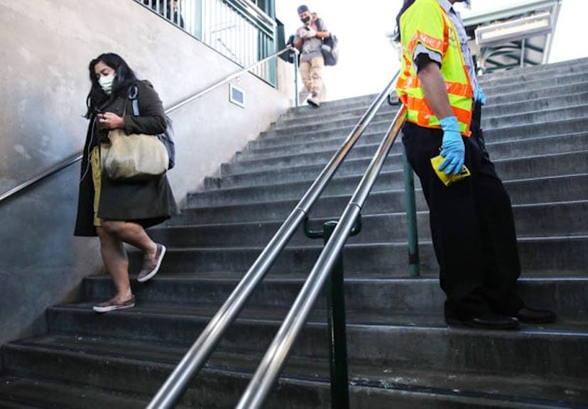 An employee wears gloves as riders descend from a Los Angeles Metro Rail train platform while wearin...