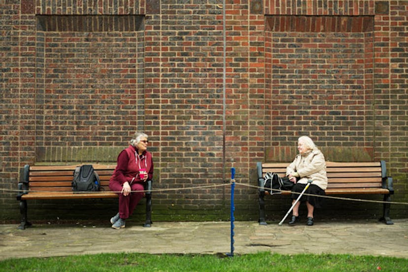Two women observe social distancing measures as they speak to each other from adjacent park benches ...