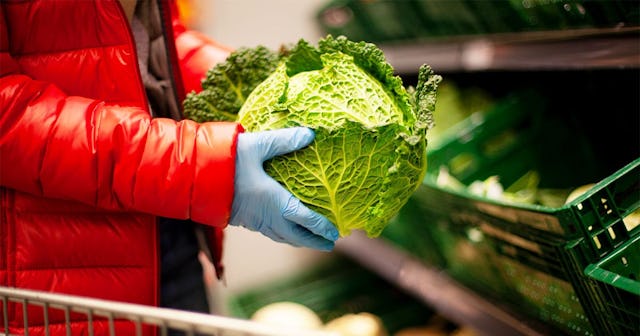 Woman picking out cabbage at the supermarket, wearing protective gloves
