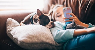girl using her mobile phone while lying on sofa with her dogs