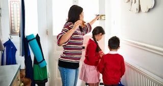 A woman opening the entrance door for her kids to leave the house