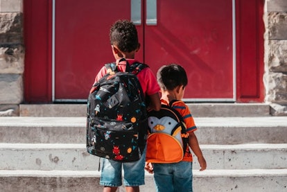 Two children huddle together in front of the school doors.