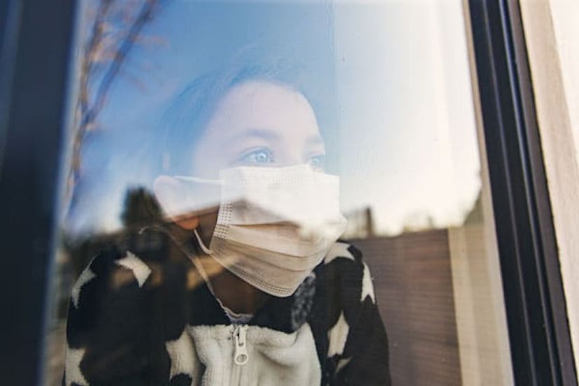 Young girl with mask looking through window