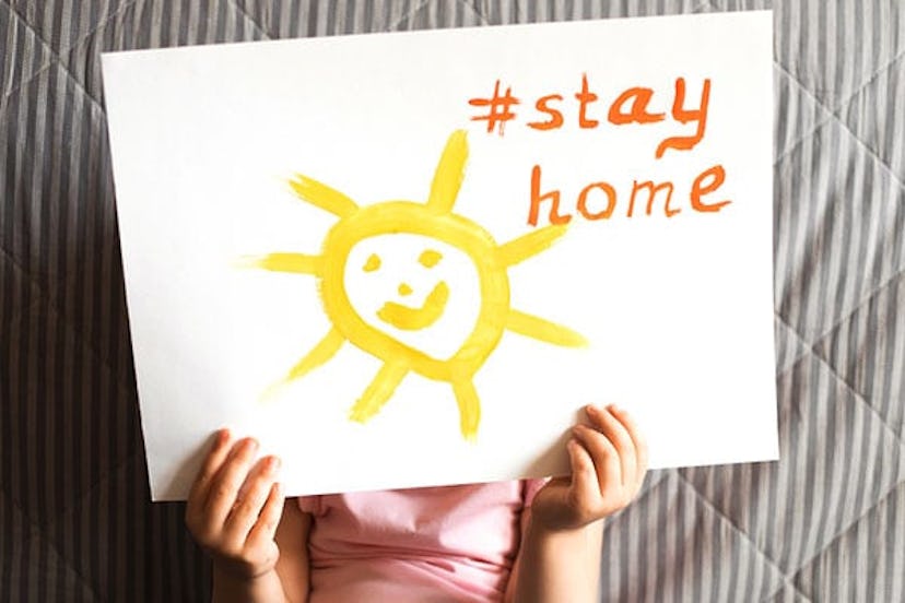 Close up of child's hands holding a piece of paper with text Stay Home and sun