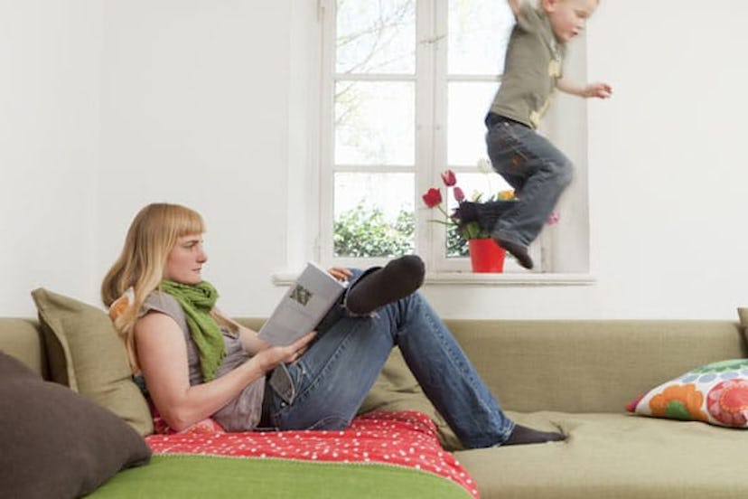 Mother relaxing as son jumps on sofa