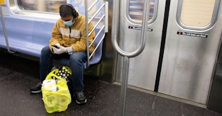 A man wearing a face mask is seen sitting on the NYC subway with a grocery bag full of toilet paper ...