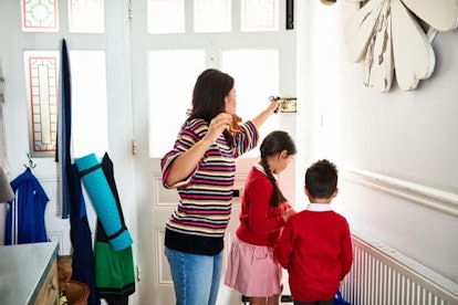 Mother eating toast and opening front door for two school children