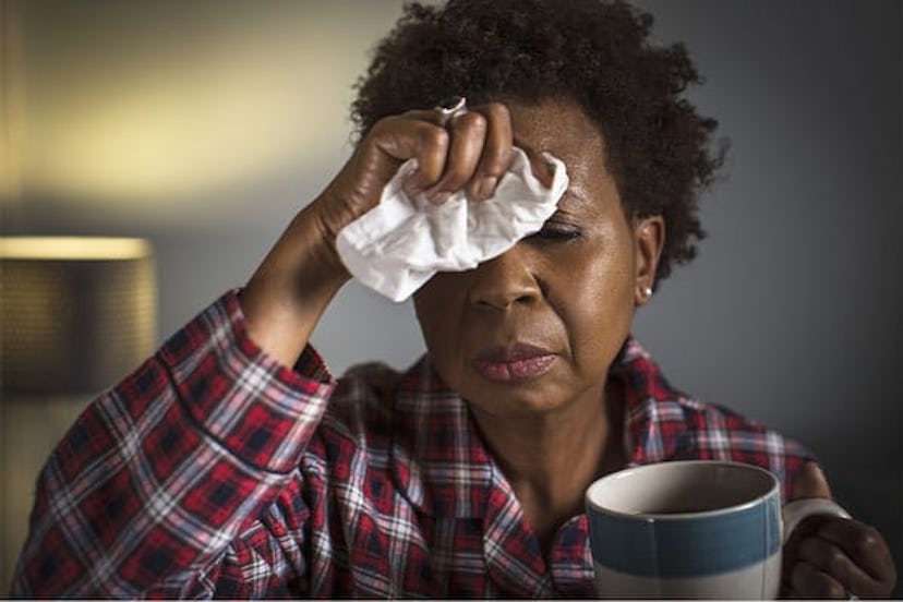 Black woman with a cold wearing red and white pajamas while holding a tissue and a cup