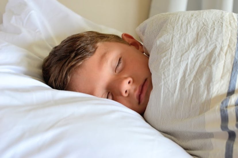 A boy lying down and sleeping on a white pillow covered with a white blanket