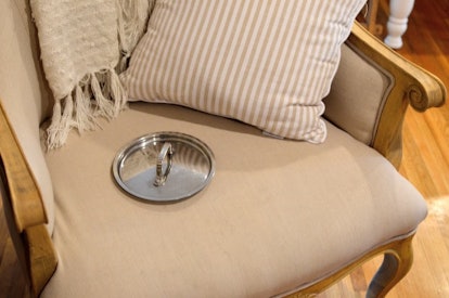 An old fashioned wooden chair with pillows on it and a silver pot lid