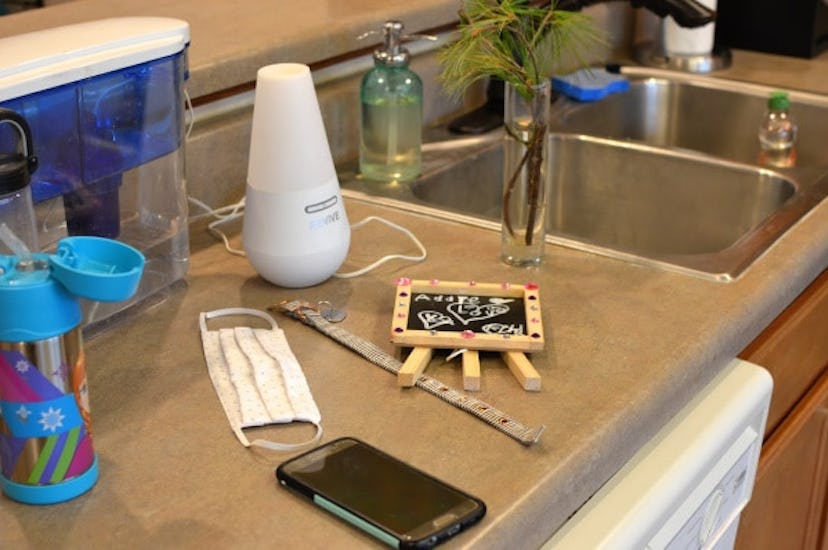 Kitchen counter with a mask, mobile phone, kitchen timer, plant and a small writing table on it