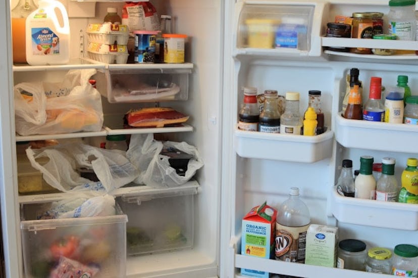 An open white refrigerator overfilled with groceries and plastic bags