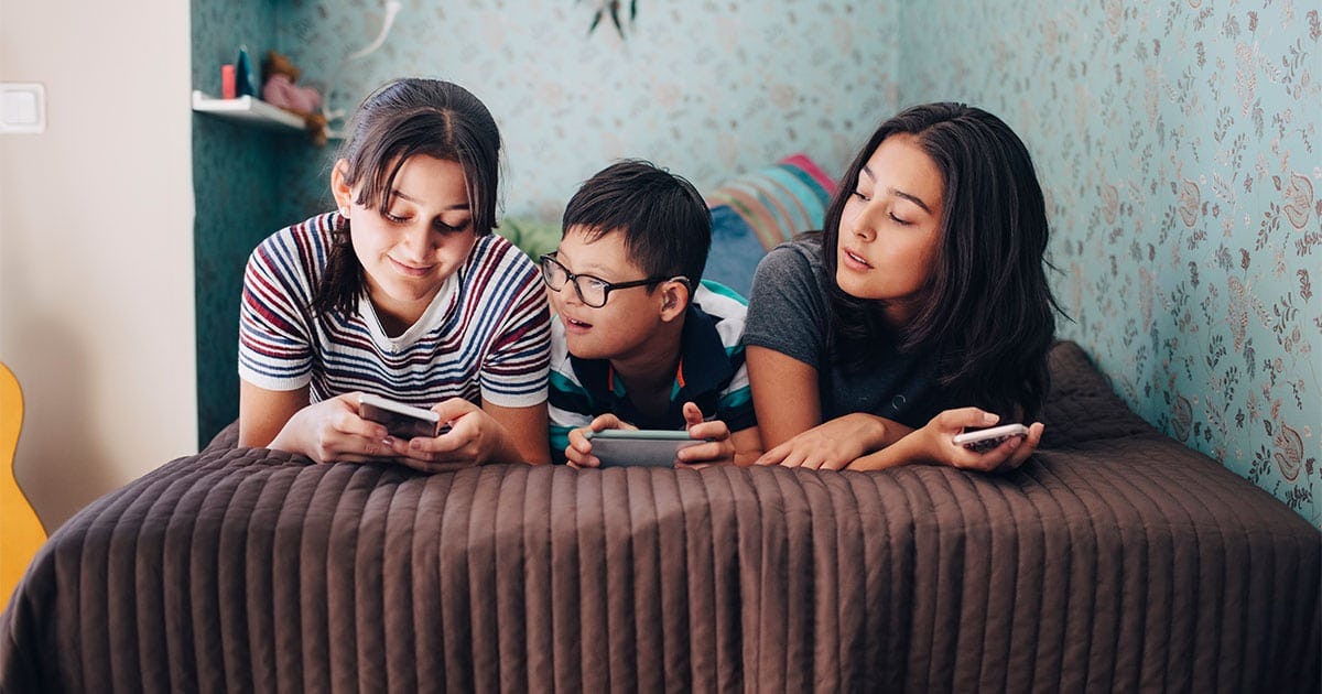 Siblings using wireless technologies while lying on bed by wall at home