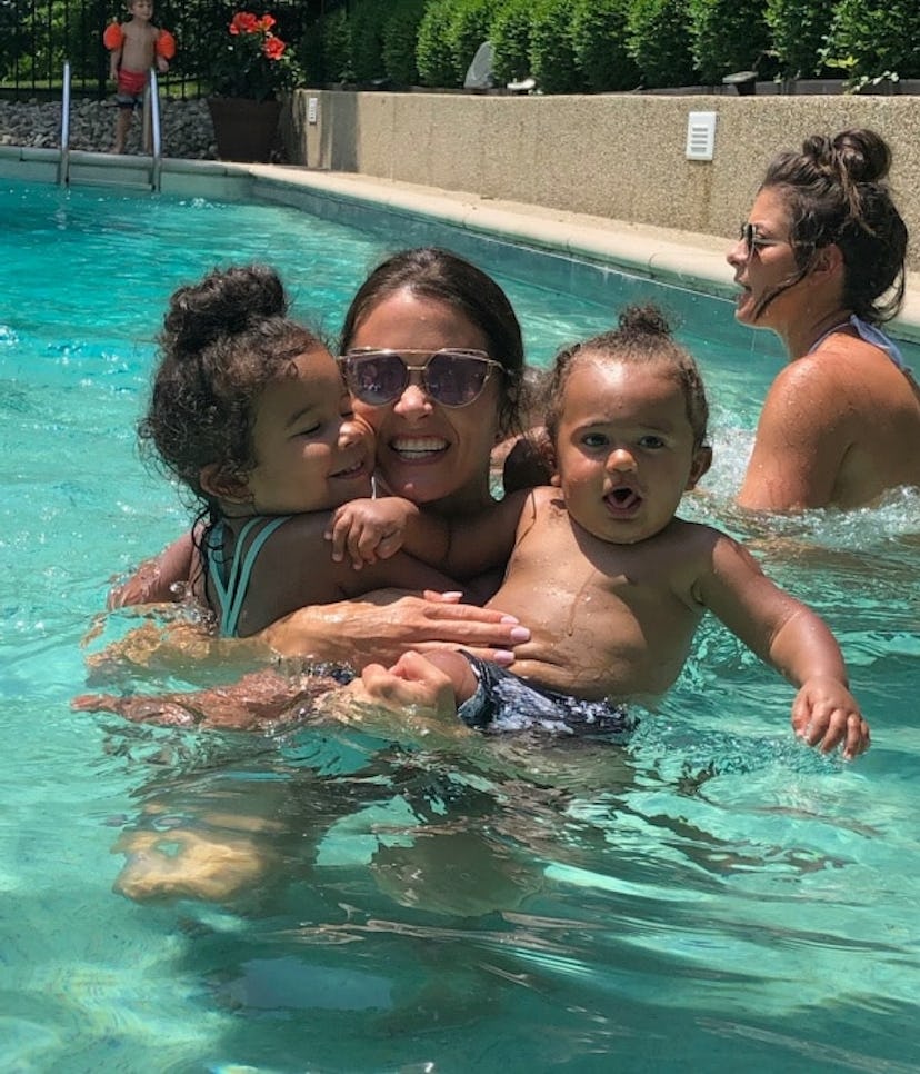 A mother holding her two babies in a pool