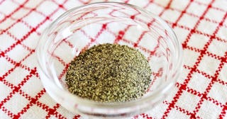 A see-through bowl of ground pepper placed on a checkered tablecloth
