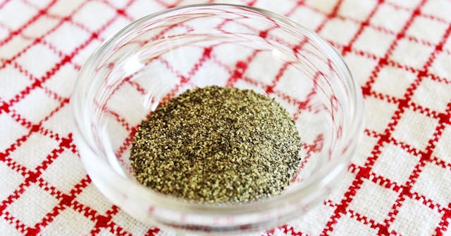 A see-through bowl of ground pepper placed on a checkered tablecloth