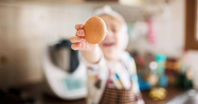 Boy in kitchen wearing a chef had and apron holding and egg in front of face