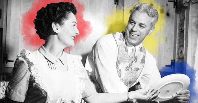 1950s SMILING HUSBAND IN APRON IN KITCHEN WASHING DISHES AS HAPPY WIFE DRIES