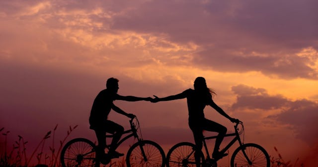 Couple holding hands while riding bikes at sunset