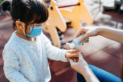Young mother squeezing hand sanitizer onto little daughter's hand in the playground to prevent the s...