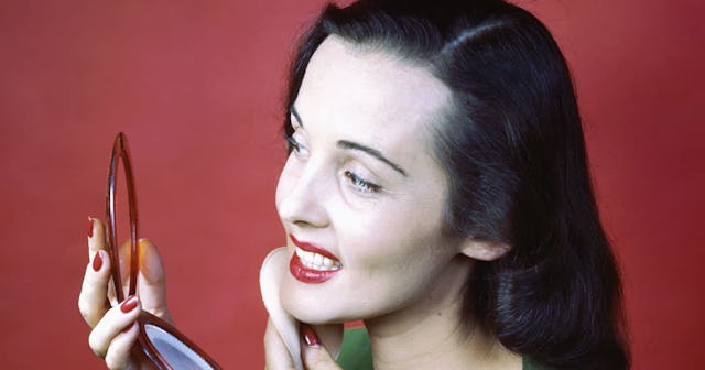 A woman holding a face powder compact with a mirror