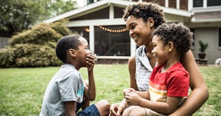 mother playing with young sons in front of house