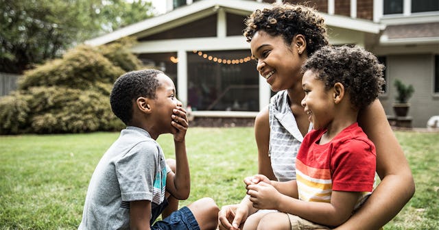 mother playing with young sons in front of house