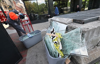 A man collects broken glass from storefront windows in tubs as people begin cleaning up in Downtown ...