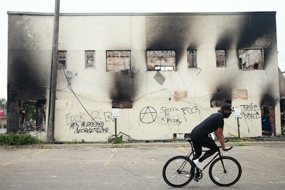 A man rides a bicycle past a burned out building after a night of protests and violence on May 29, 2...