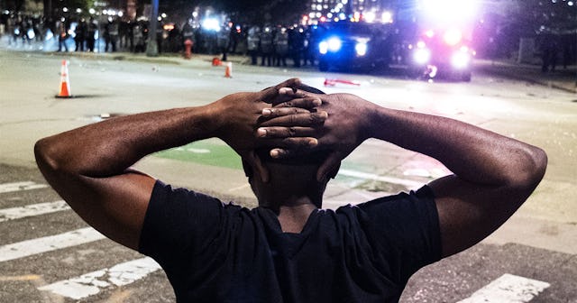 A protester holds his hands on his head in front of a formation of Detroit riot police,as protesters...