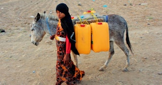 A girl walks with a donkey carrying jerry cans filled with water from a cistern at a make-shift camp...