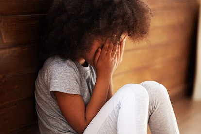 Upset african american child girl crying sitting alone on floor