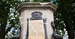 A close-up of the base of the Edward Colston statue plinth with a taped-on cardboard message saying ...