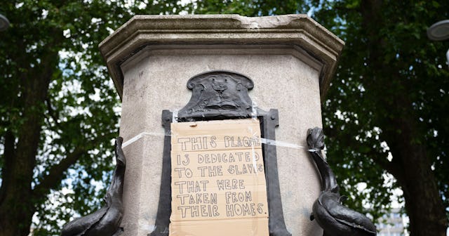 A close-up of the base of the Edward Colston statue plinth with a taped-on cardboard message saying ...