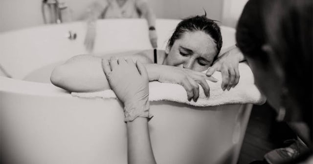 A woman giving birth in the bathtub while another woman is touching her arm, comforting her