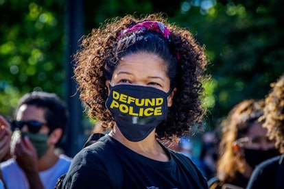 A participant wearing a face mask with the words Defund Police in it. Thousands of protesters gather...