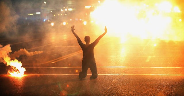 Tear gas reigns down on a woman kneeling in the street with her hands in the air after a demonstrati...