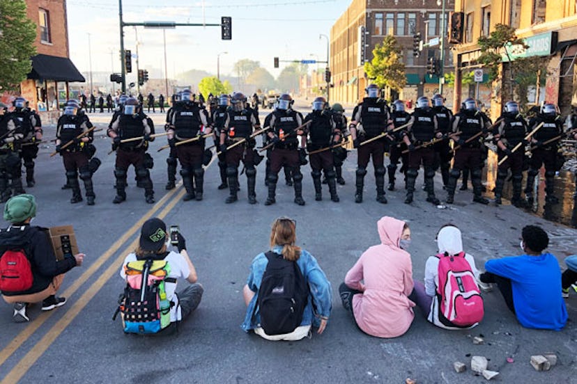 People sit on the street in front of a row of police officers during a rally in Minneapolis, Minneso...