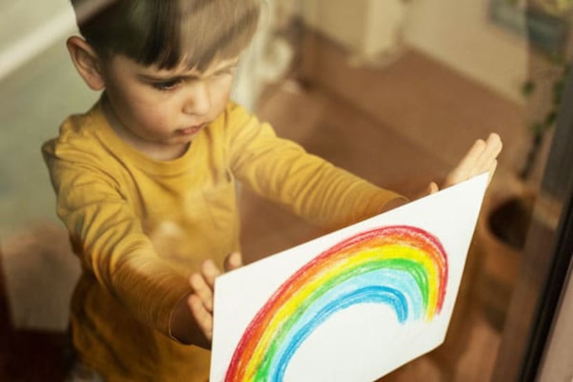 Kid holding a drawing of a rainbow through the window