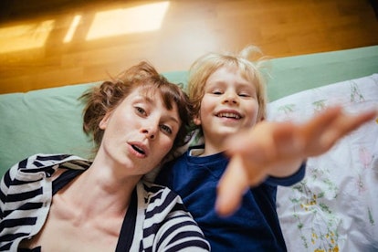 Mother and little son lying on bed reaching out to camera