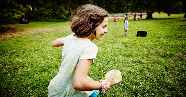 Girl running through field with water balloon